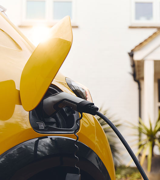 Sarı elektrikli araç, evin önünde şarj ediliyor. Ev tipi şarj istasyonu kullanımı.